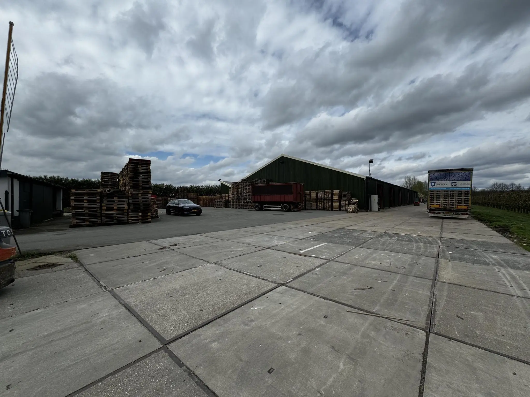 Opslagterrein met houten pallets, vrachtwagens en een loods aan de Graaf van Lynden van Sandenburgweg.